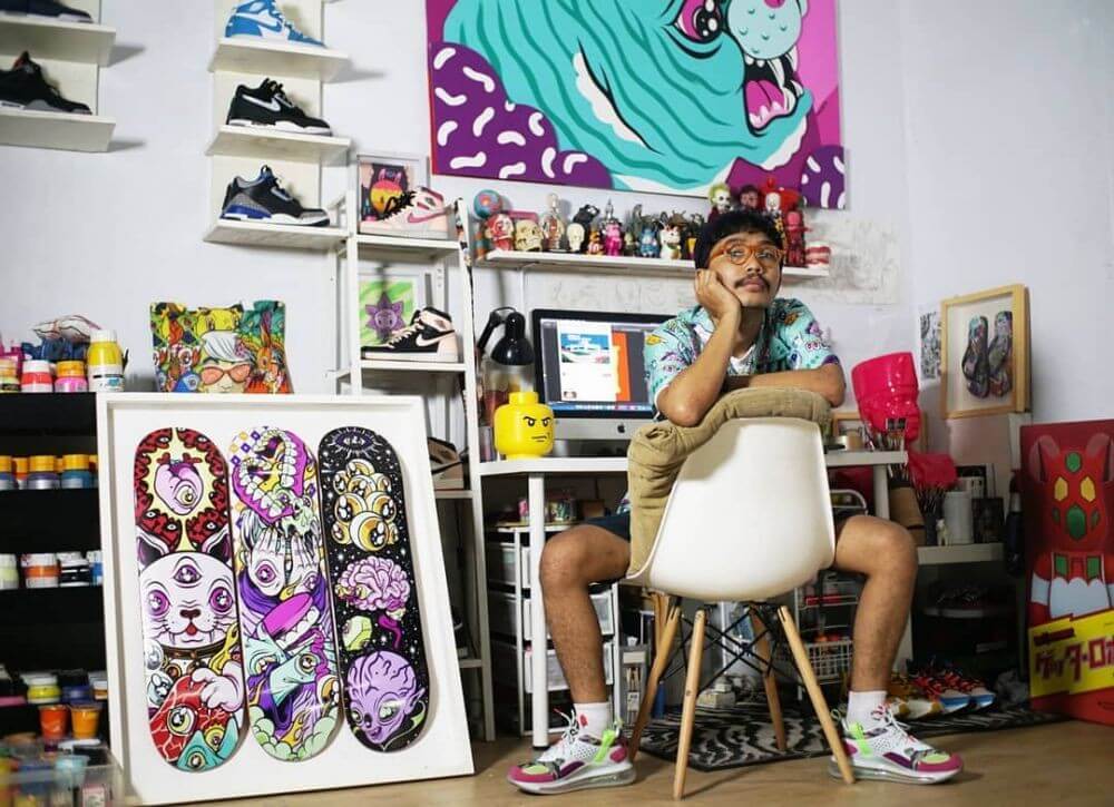 Muklay mengenakan ensemble warna-warni sedang duduk di atas bangku putih